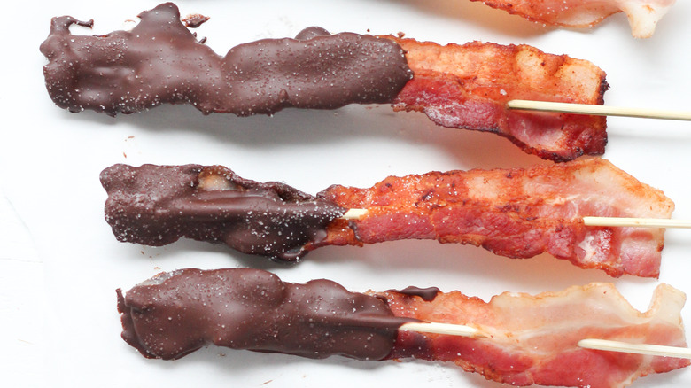 Three slices of chocolate-covered bacon on a stick