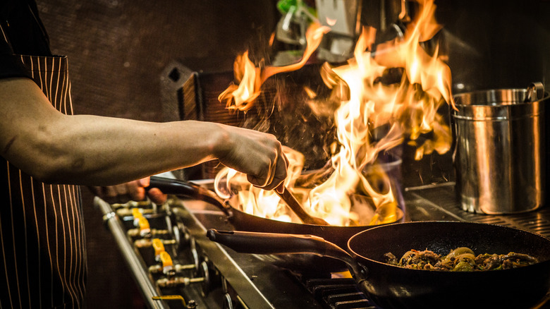 A chef cooks on a stove, with a hot wok full of flames
