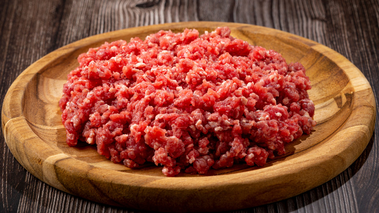 Raw ground beef on a round wooden plate.