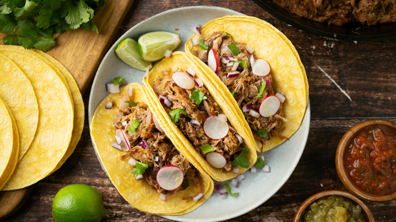 three carnitas tacos on white plate with lime wedges