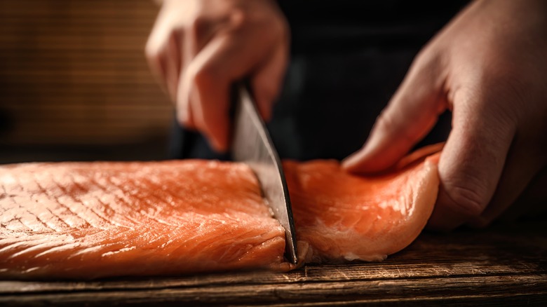 chef cuts salmon fillet with knife