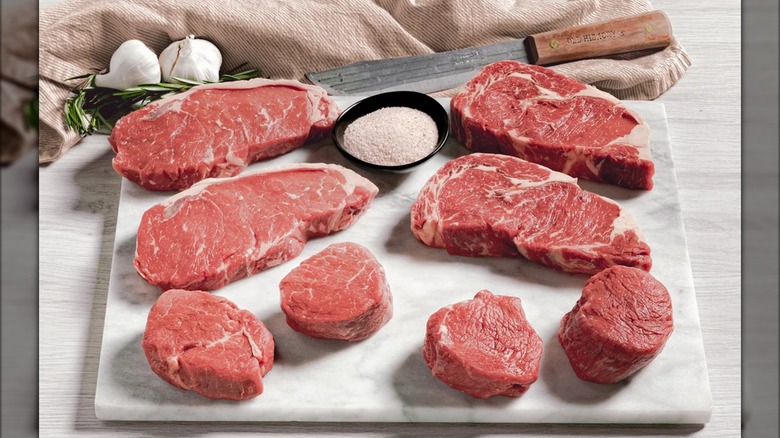 Two New York strip steaks, two boneless ribeyes, two filets mignon, and two sirloin steaks with bowl of pink salt.