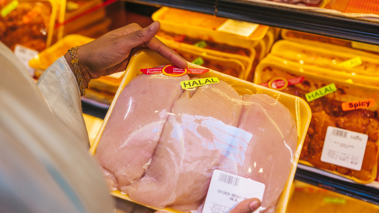 A person holding a package of chicken breasts in the grocery store labeled halal