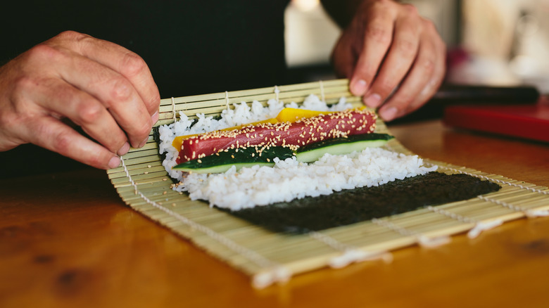 Person rolling sushi with sushi mat