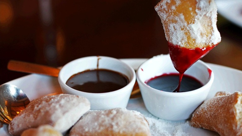 Zeppole being dipped in raspberry sauce