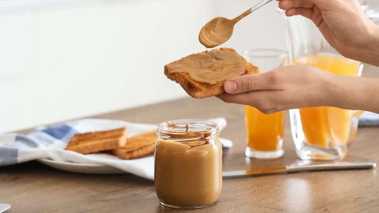 Spreading peanut butter on toast with orange juice in background