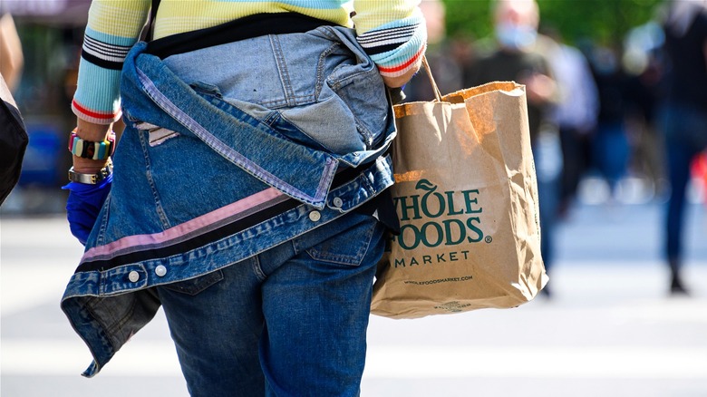 Person carrying Whole Foods brown bag 