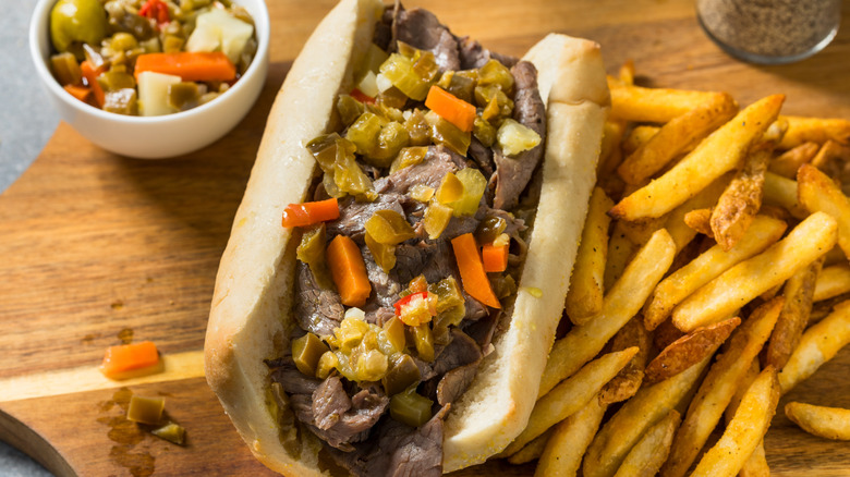 Italian beef sandwich with extra giardiniera on the side and french fries on a wooden board
