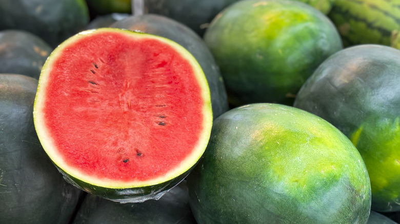 A halved watermelon sits amongst several whole melons