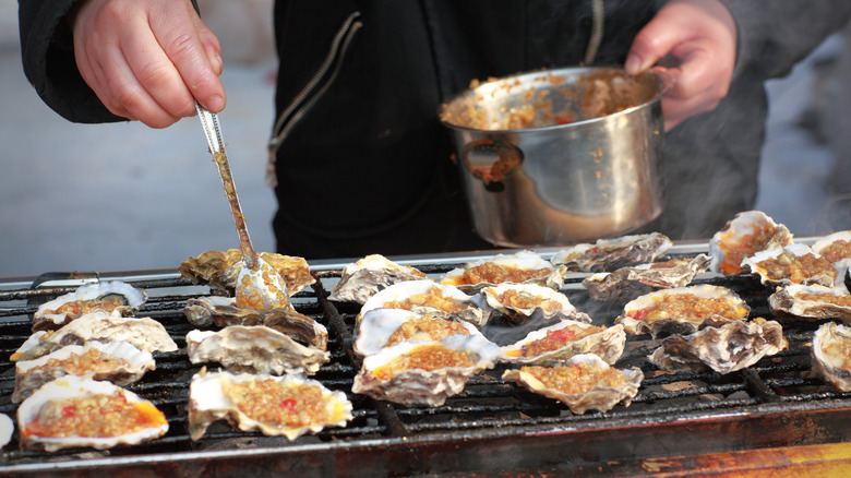 Person brushing oysters on grill