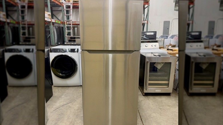 A silver Insignia refrigerator in a warehouse with other home appliances