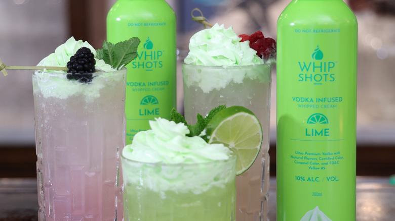 Cans of Whipshots next to cocktails topped with the product