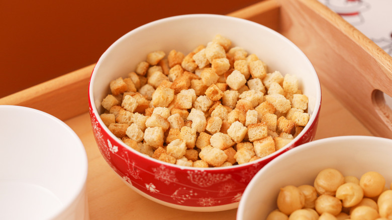 Croutons sitting in a red and white nowl next to a bowl of chickpeas
