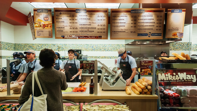 Inside a Jersey Mike's as employees prepare food and a customer orders