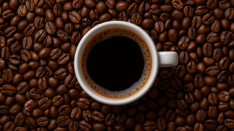 A top view of a cup of black coffee surrounded by coffee beans
