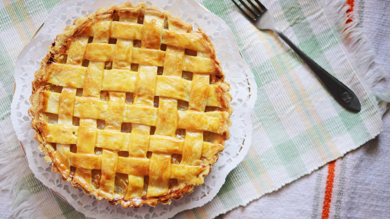 A fully baked pineapple ie with a lattice pie crust on top of it next to a fork