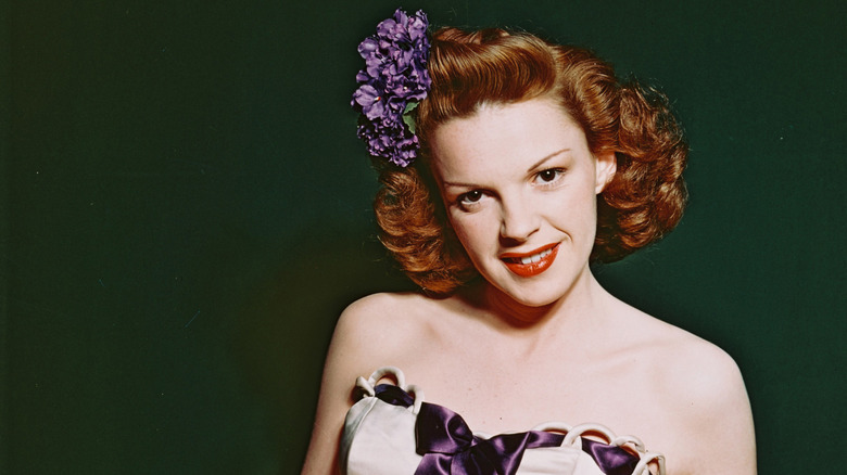 Actress Judy Garland with a purple flower on her head and a green background