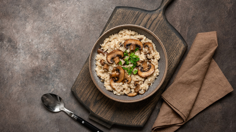 Rustic bowl filled with mushroom risotto on a wooden cutting board