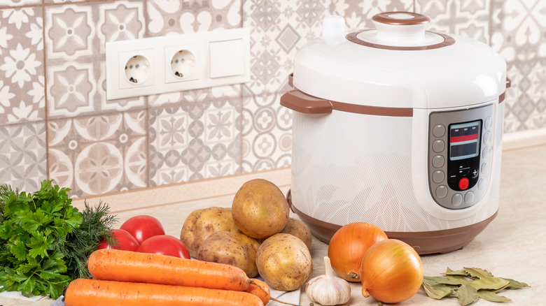 A slow cooker on a kitchen sideboard, with vegetables next to it