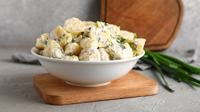 Potato salad with herbs in a white bowl on a wood cutting board