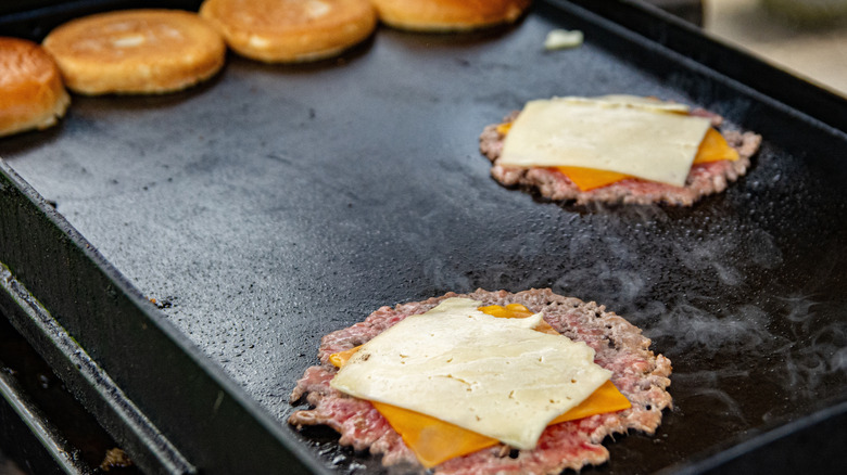 Smash burgers being cooked on a griddle