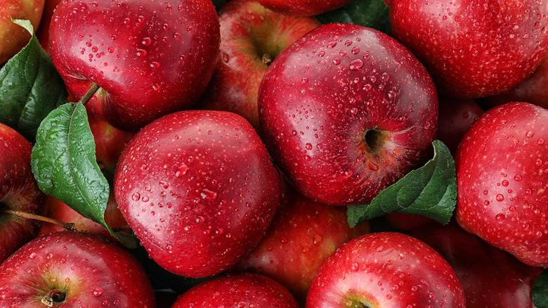 A pile of fresh red apples, some of which still have their green leafy stem attached