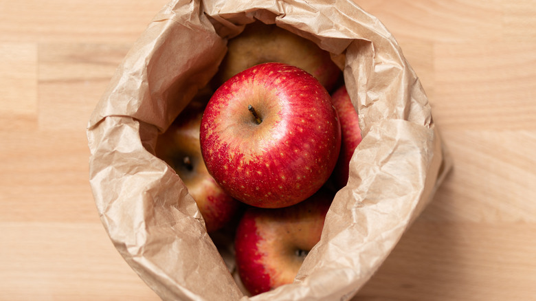 A top-down view of several apples piled inside a large paper bag