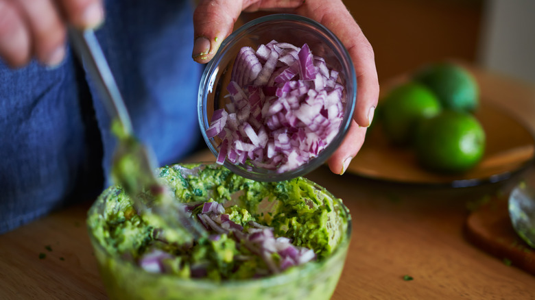 hands adding onions to guacamole