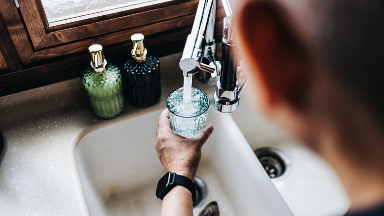 Hand filling a glass with water over a sink