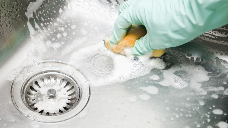 Green-gloved hand using a sponge to clean a kitchen sink