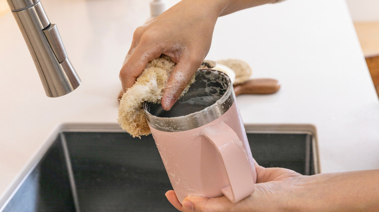 Hands washing pink metal tumbler in sink