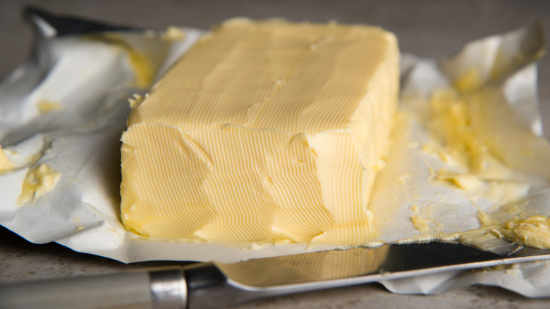 A stick of butter on its wrapper that has been scraped with a butter knife
