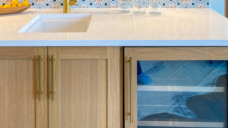 A colorful, patterned vinyl backsplash behind a white surface and gold faucet.