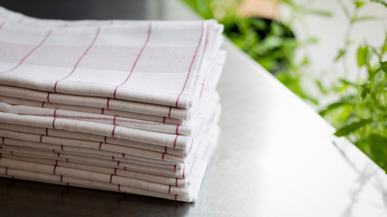 A stack of white towels with red stripes next to green plants