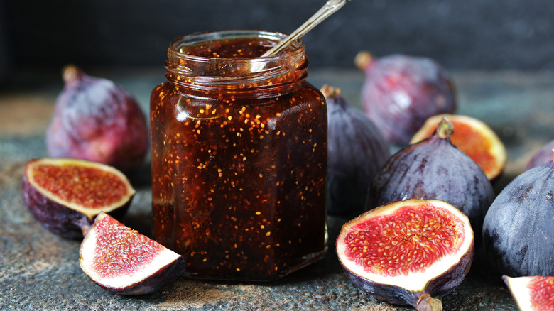 Fig marmalade in jar with spoon, surrounded by cut figs