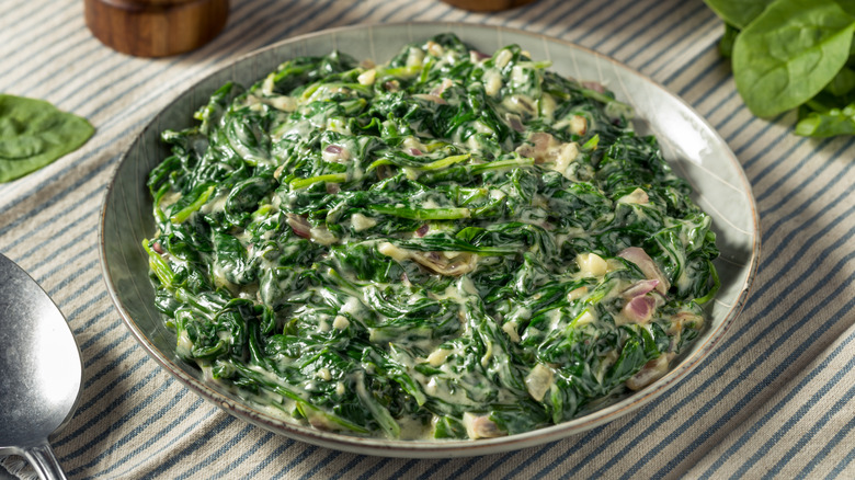 Plated creamed spinach next to spoon and fresh spinach leaves
