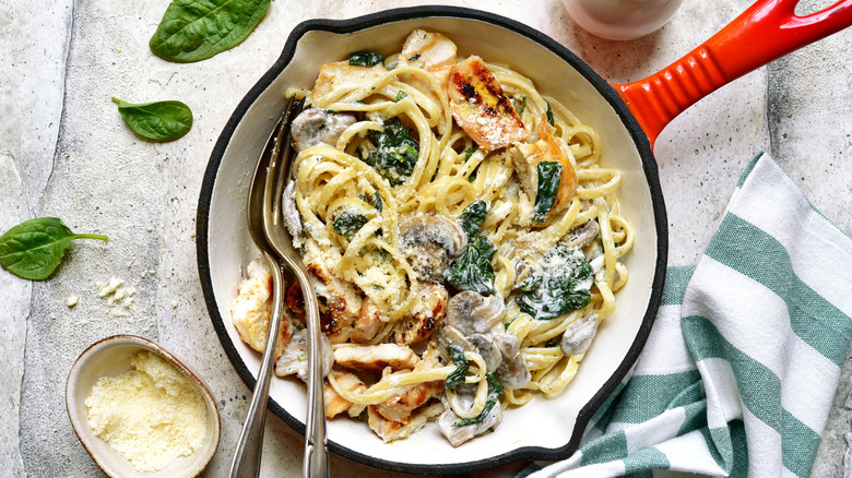 Creamed spinach pasta with chicken and mushrooms in a pan with spoon and fork