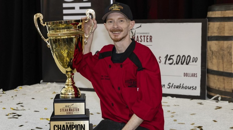 LongHorn Steakhouse Steak Master Series 2025 Champion Tim Crain wearing a red shirt and sitting next to a large gold trophy