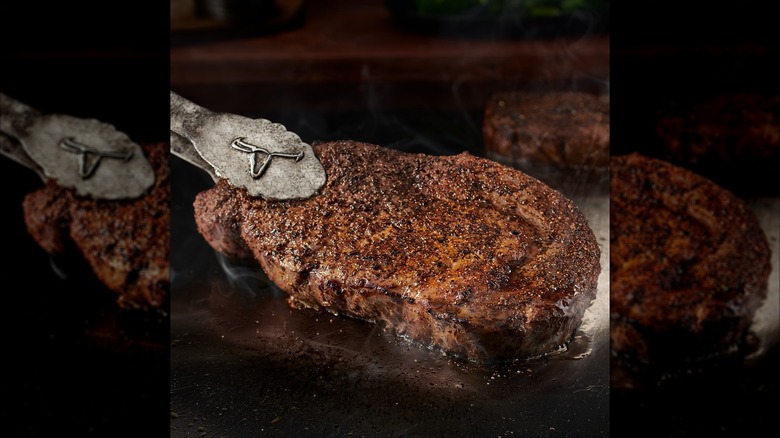Ribeye being held on one side with LongHorn-logoed tongs