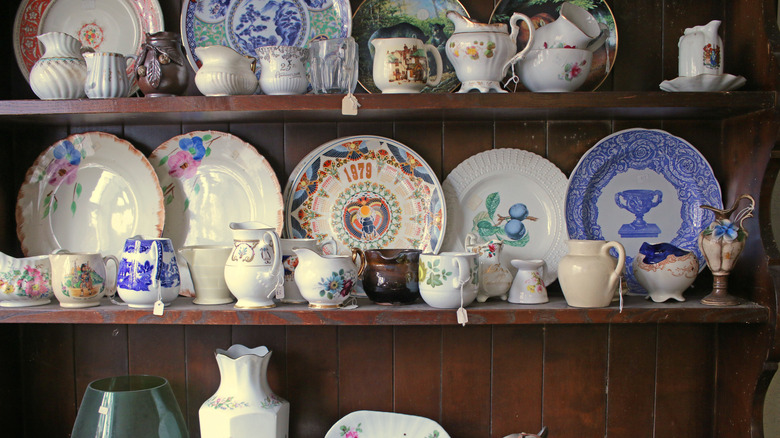 An antique store shelf with assorted cups, bowls, dishes, and serving wares.