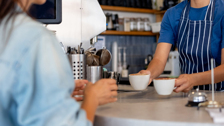a smiling barista handing someone their drinks