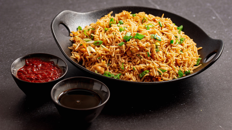 A black bowl of fried rice next to two cups of sauces