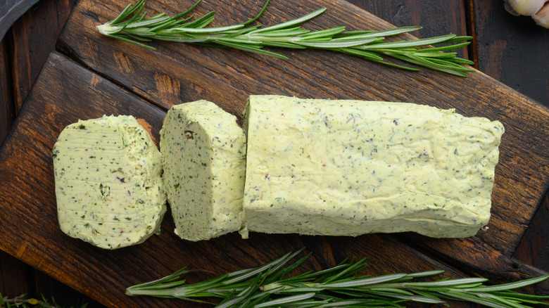 Herb infused compound butter next to herbs on a wooden surface
