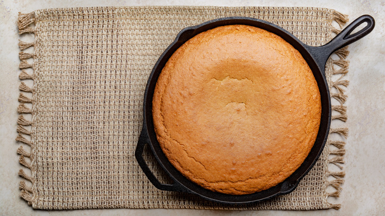 Top view of a cast iron skillet with cornbread inside on top of a burlap placemat