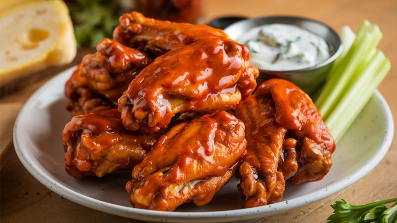 Close up of buffalo wings on a white plate with dipping sauce and celery sticks