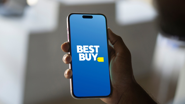 A hand holding a phone with the Best Buy logo displayed on the screen
