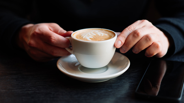 Hands holding a cup of Nespresso cappuccino over a saucer