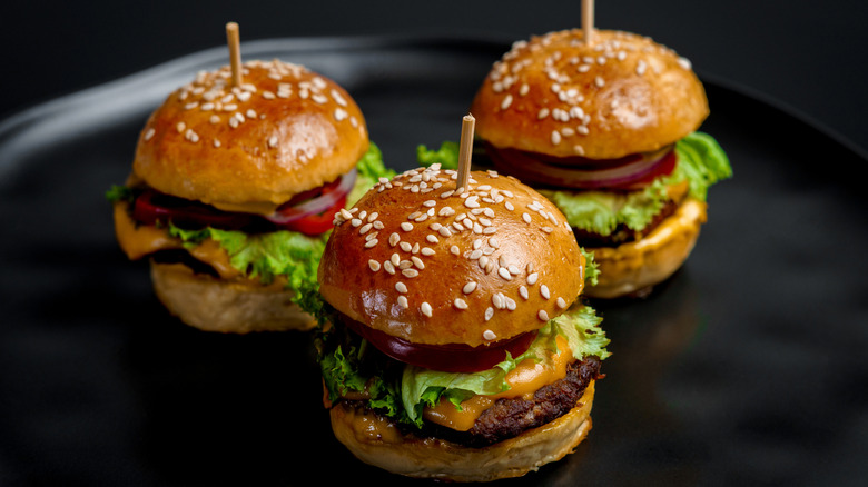 Three sliders with lettuce, onion, and cheese