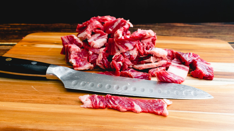 Thin sliced of ribeye on a wood cutting board with a kitchen knife