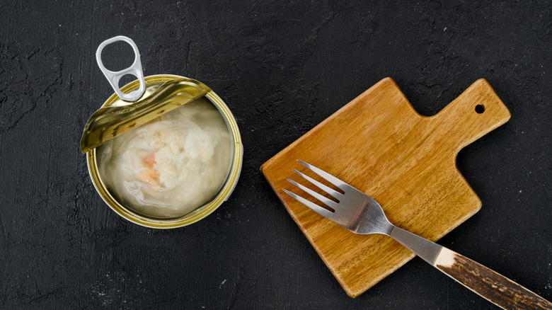 canned crab meat next to fork on wooden board